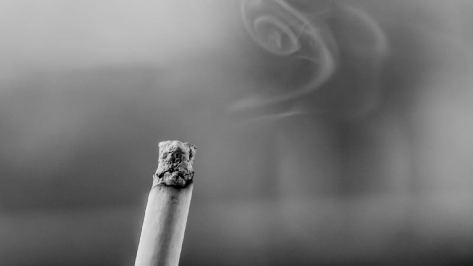 Ασπρόμαυρη φωτογραφία αναμμένου τσιγάρου και καπνού.